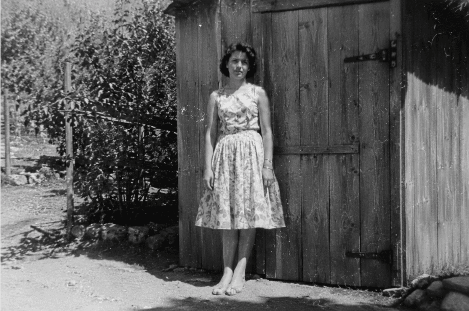 A young woman standing in a shed doorway, black and white.